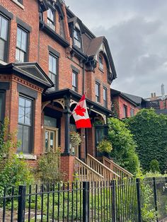 a red brick house with a canadian flag hanging from it's front door and black iron fence