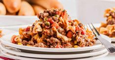 a white plate topped with pasta covered in ground beef and veggies next to bread