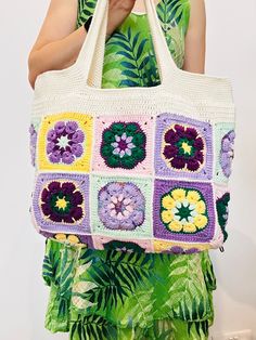 a woman holding a crocheted bag with flowers on it