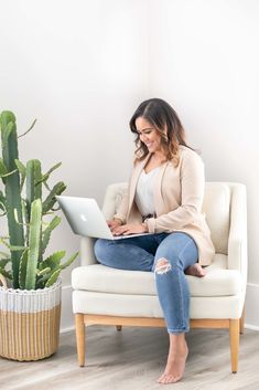 a woman sitting on a chair with a laptop in her lap and potted plant behind her