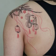 a woman's back with tattoos on her body and flowers hanging from the strings