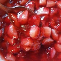 a spoon in a bowl filled with strawberries and jelly sauce on top of it