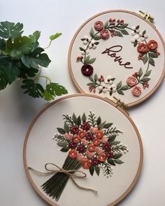 two embroidered hoops with flowers and the words love on them, one is holding a plant