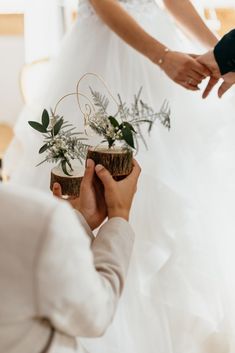 the bride is holding a small planter with greenery on it while her groom holds his hand