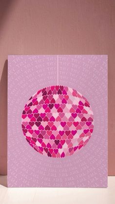 a pink card with hearts hanging from it's side on a white table next to a wall