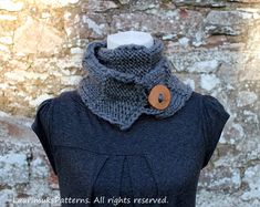 a gray cowl neck sweater with a wooden button on the collar, and a stone wall in the background