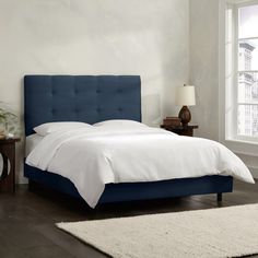 a bed with white sheets and blue headboard next to a window in a bedroom