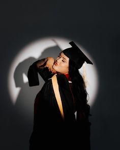 a woman wearing a graduation cap and gown in front of a shadow on the wall