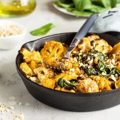 a skillet filled with cauliflower and spinach on top of a table