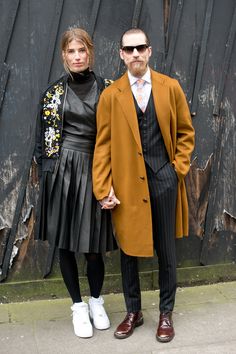 two people standing next to each other in front of a wall