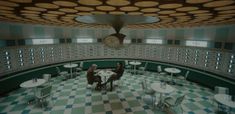 two people sitting at a table in a room with checkered floor and circular ceiling