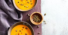 two bowls of carrot soup with seeds in them