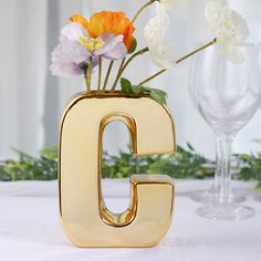 there is a vase with flowers in it and the letter c on the table next to two wine glasses