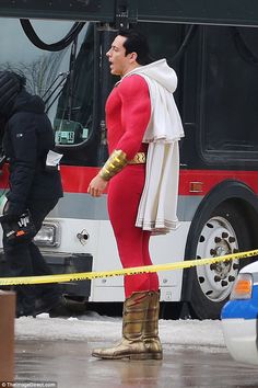 a man in a red costume standing next to a bus