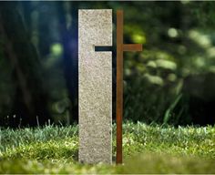 a wooden cross sitting in the grass next to a stone pillar with a black cross on it