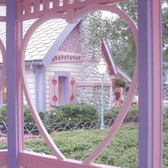 a heart shaped window frame in front of a pink house with a white picket fence