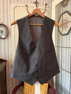 This classic vest is made from a wool blend in a very small charcoal grey and black houndstooth check. It has the original buttons in the front and four front pockets, and is fully lined with dark grey silky lining. The back matches the lining. The measurements, taken with the vest lying flat, are: shoulder to shoulder, 14 inches; armpit to armpit, 22 inches; length, 26 inches in front and 23 inches in back; bottom edge, 22 inches. In very good condition. Wool Business Vest For Fall, Wool Vest For Business In Fall, Classic Tailored Gray Vest, Classic Business Vest For Winter, Gray Winter Workwear Vest, Classic Wool Vest For Winter, Classic Wool Winter Vest, Classic Gray Vest For Work, Winter Classic Wool Vest