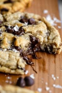 two chocolate chip cookies on a cutting board with one broken in half and the other partially eaten