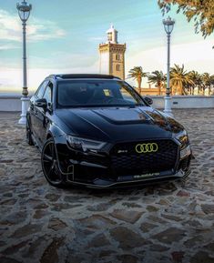 a black car parked in front of a clock tower on a cobblestone road