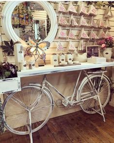 a bicycle parked next to a table with flowers on it and a mirror above it