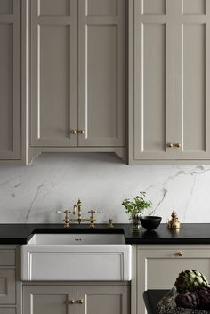 a kitchen with gray cabinets and black counter tops, gold pulls on the faucet