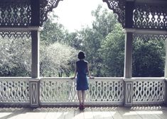 a woman in a blue dress is standing on a white porch looking out at the trees