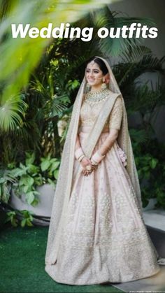 a woman in a white and gold bridal gown posing for the camera with greenery behind her