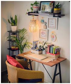 a desk with some plants and pictures on the wall above it, along with two wicker chairs