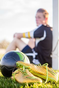 a woman sitting in the grass next to a soccer ball and boot on the ground