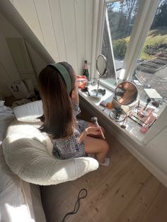 a woman sitting in front of a window holding a toothbrush and looking out the window