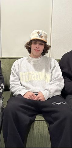 a young man sitting on top of a green couch wearing a white and yellow hat