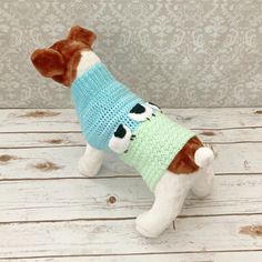 a stuffed dog wearing a sweater on top of a wooden table next to a wall