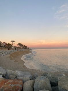 the beach is lined with large rocks and people walking on it at sunset or dawn