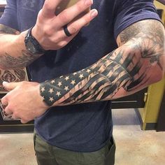 a man with an american flag tattoo on his arm and arms is holding a cell phone