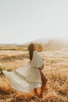 a woman in a white dress is standing in a field with her legs spread out