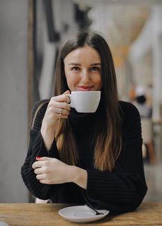 a woman sitting at a table with a cup in her hand and looking into the camera