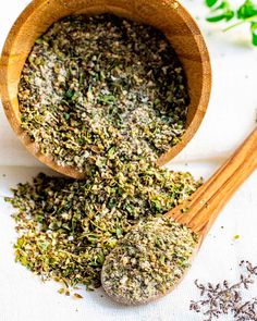 two wooden spoons filled with herbs on top of a table