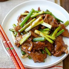 a white plate topped with meat and veggies next to chopsticks