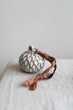 a white vase sitting on top of a bed next to a tasselled pillow