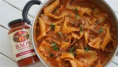 a pot filled with pasta and sauce next to a jar of hot sauce on a table