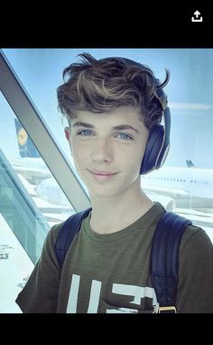 a boy with headphones on standing in front of an airport window looking at the camera