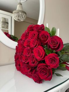 a bouquet of red roses sitting on top of a white table next to a mirror