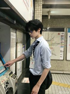 a young man standing next to a machine in a subway station, looking at the screen