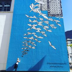 a person standing in front of a large mural on the side of a blue building