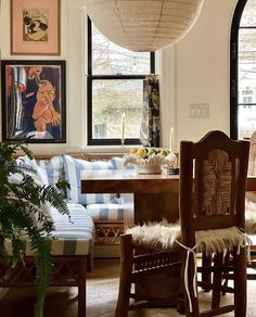 a dining room table with chairs and pictures on the wall behind it in front of two large windows