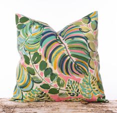 a colorful pillow on top of a wooden table next to a white wall and tree trunk