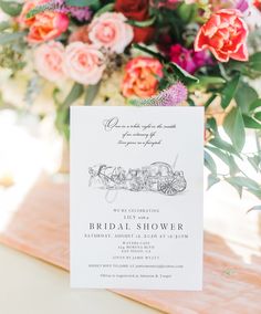 an elegant bridal shower is displayed on a table with pink flowers and greenery