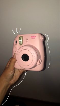 a person holding up a pink camera in front of a wall