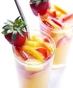 two glasses filled with fruit and garnish on top of a white table next to each other