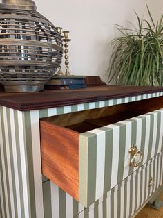 a dresser with striped drawers on top of it and a potted plant in the background